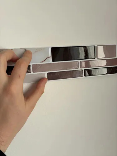 Muestras de guardas autoadhesivas mosaico 3D en tonos gris, negro y plateado sostenidas en mano