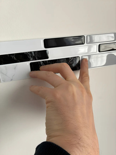 Mano tocando muestras de guardas autoadhesivas 3D en diferentes colores y patrones instaladas en pared