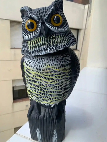 Búho espanta pájaros negro con textura punteada, ojos amarillos grandes y base cilíndrica, vista lateral completa